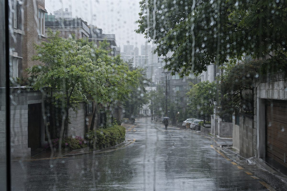 빗방울 맺힌 창 너머 젖은 주택가 골목과 우산을 쓴 행인